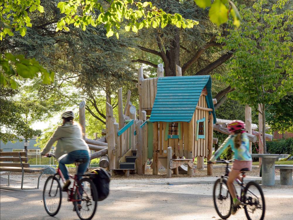 A parent and child bike past the playground.