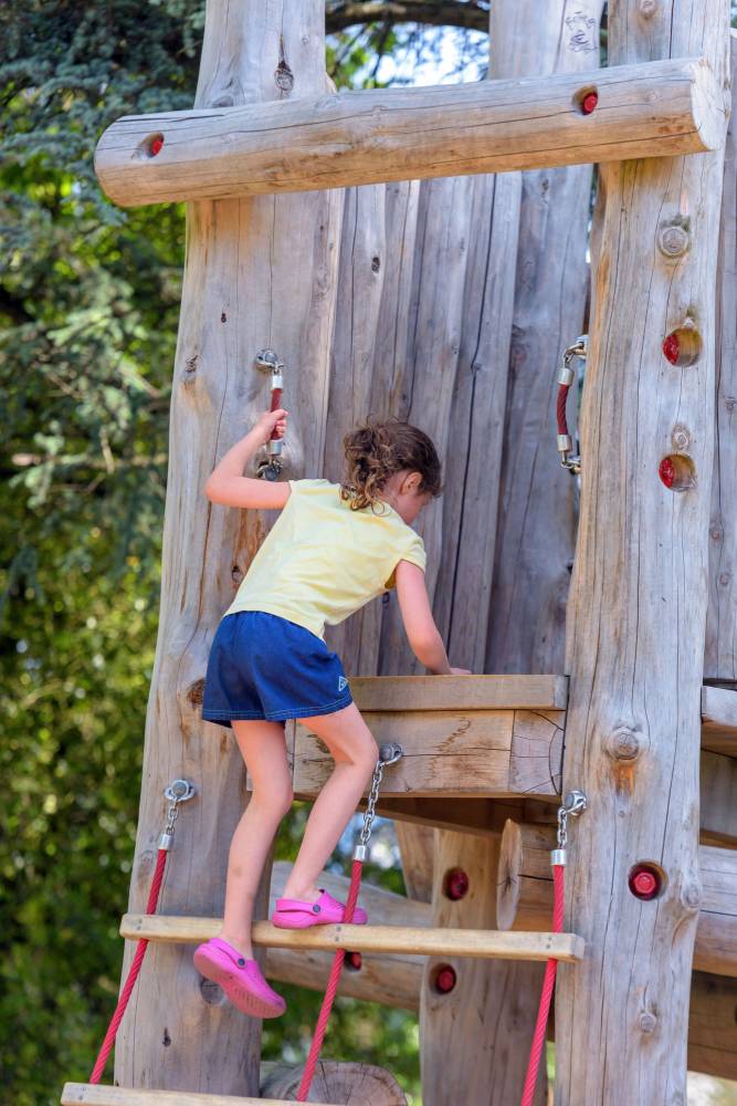 A girl climbs the central log structure on the playground.