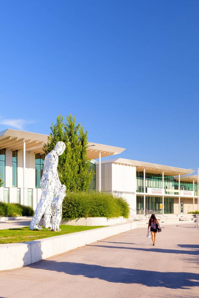 A young woman with a backpack walks towards the Aquatic Centre.