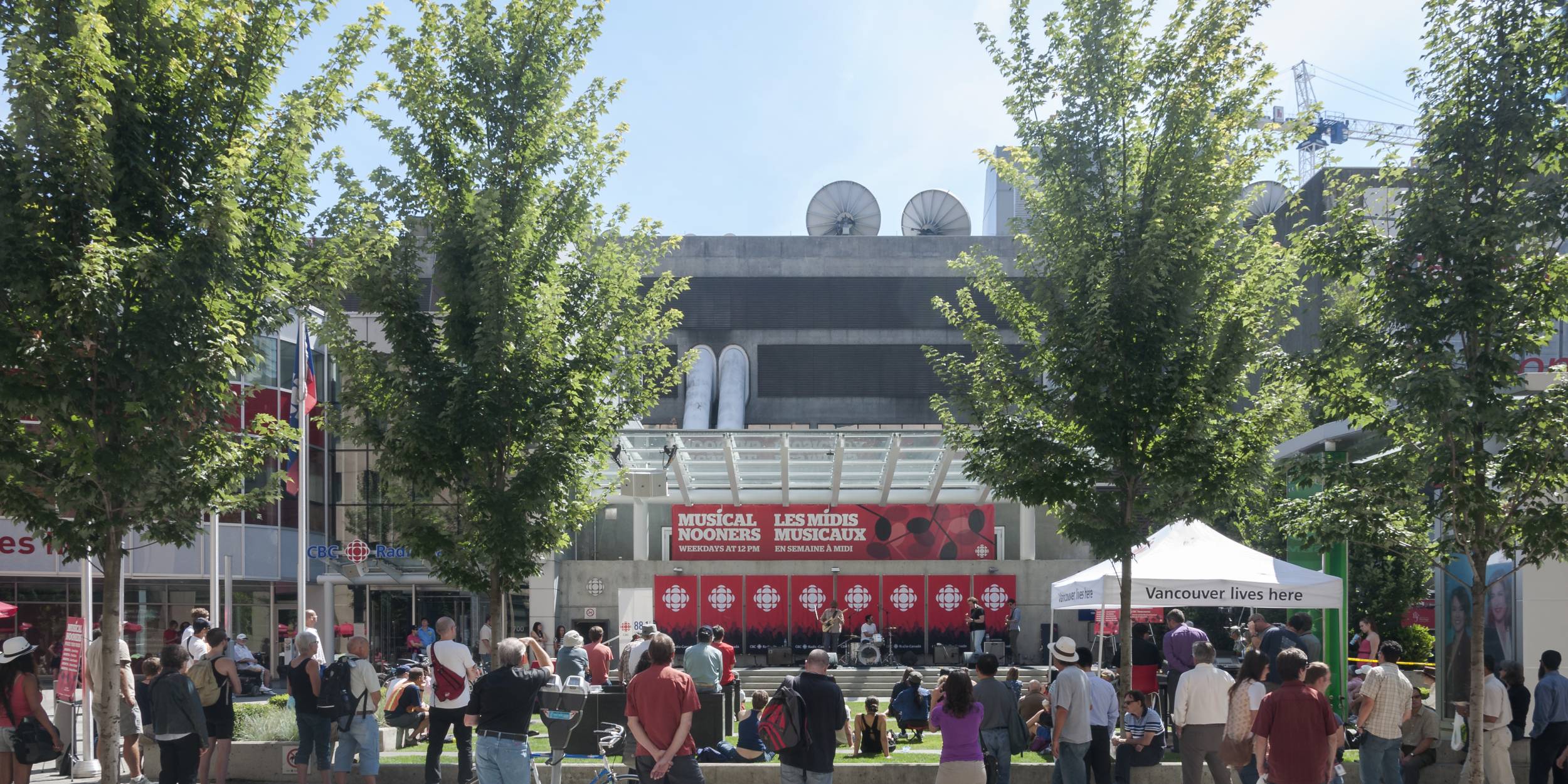 People standing in front of the plaza, which has a stage set up for lunchtime music events.