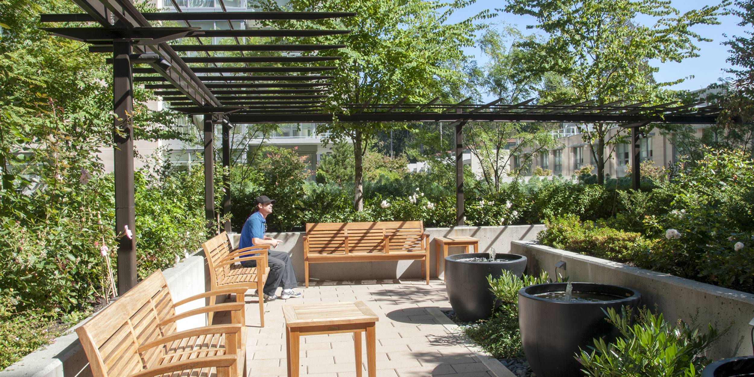 A man sits outside on a bench surrounded by the lush planting in the Tapestry Seniors outdoor space.