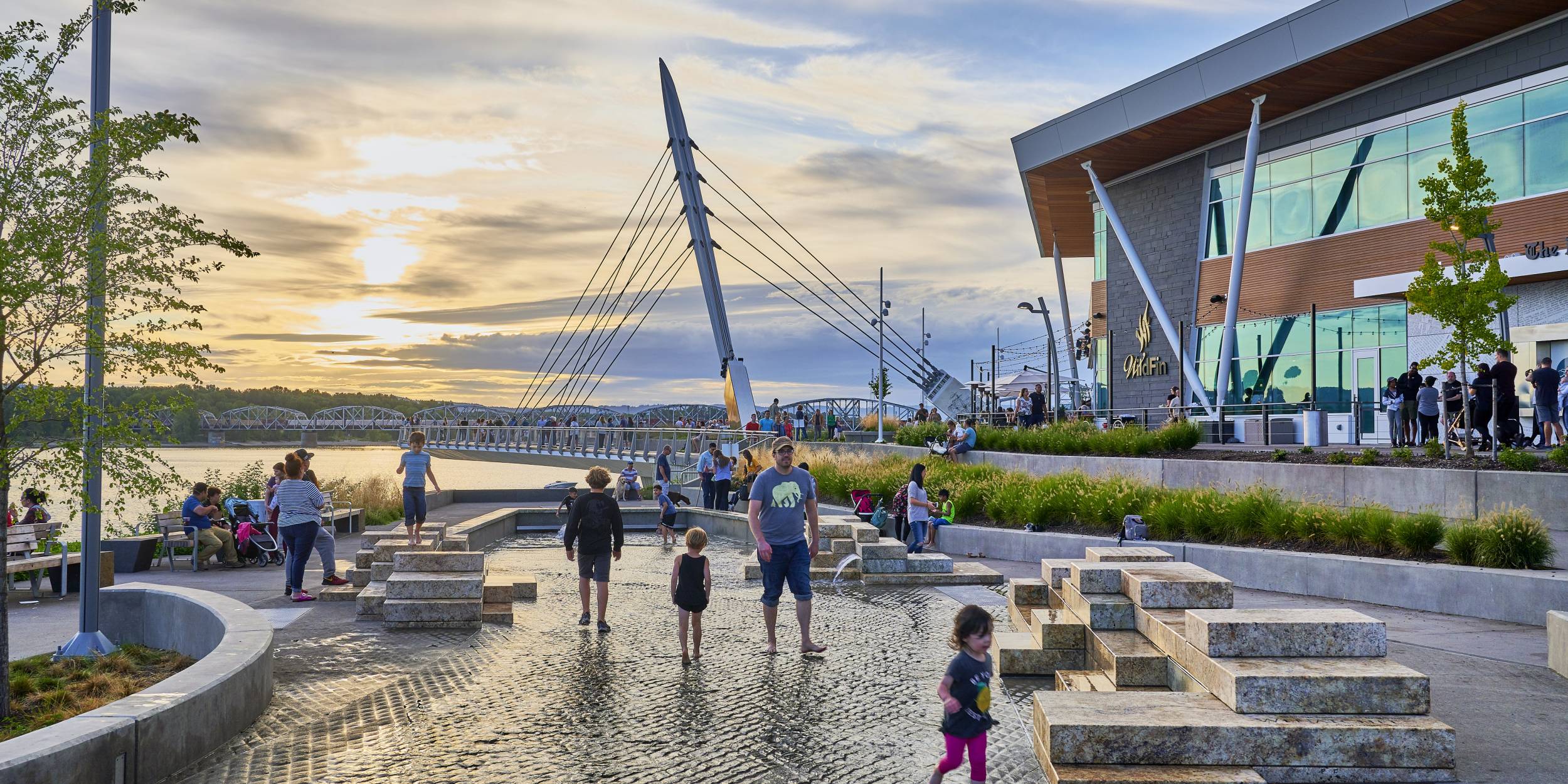 Families and kids play in the water play area of the park.