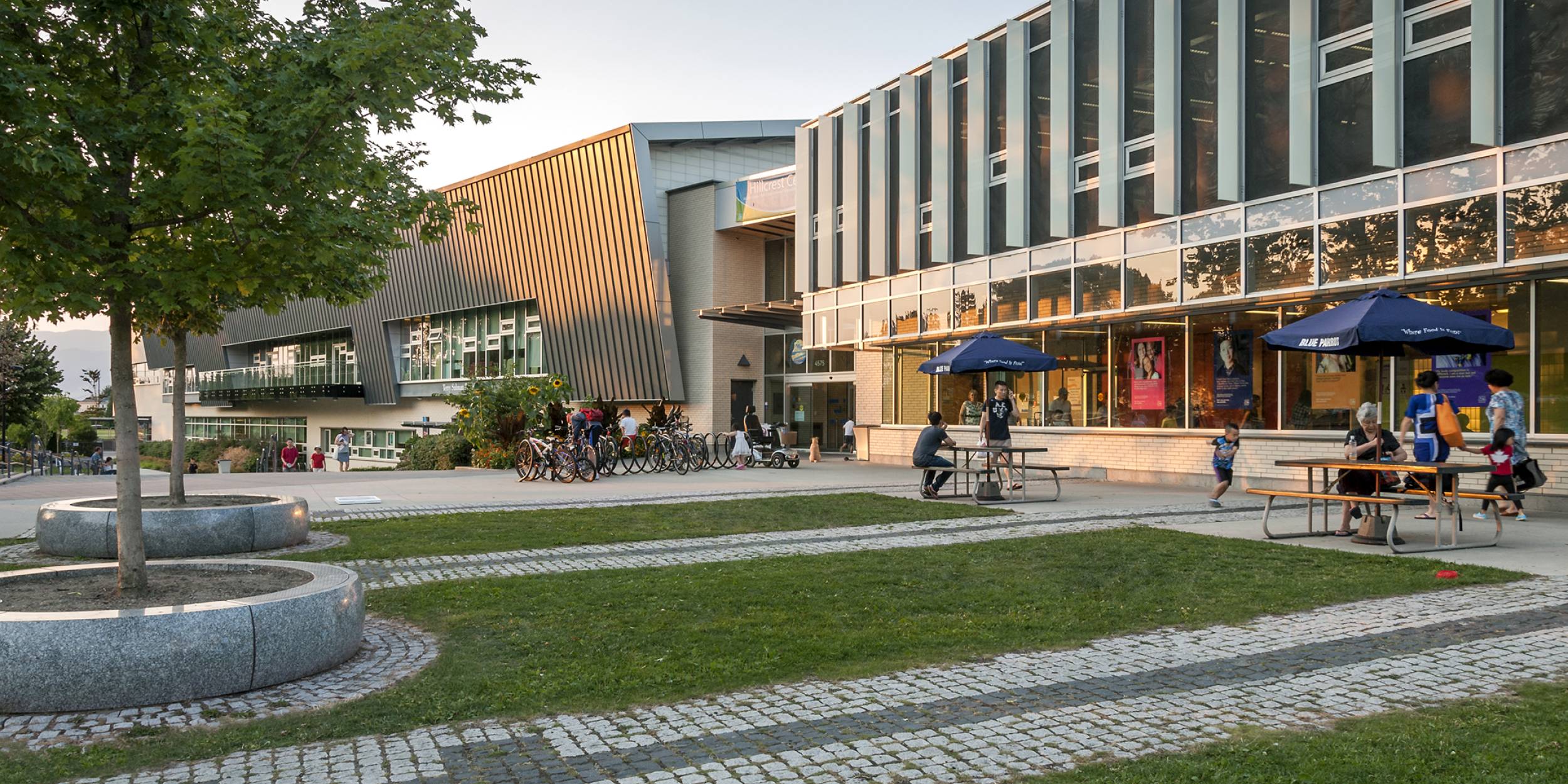 Exterior of Hillcrest Community Centre. People sit on the many shaded benches near the building.