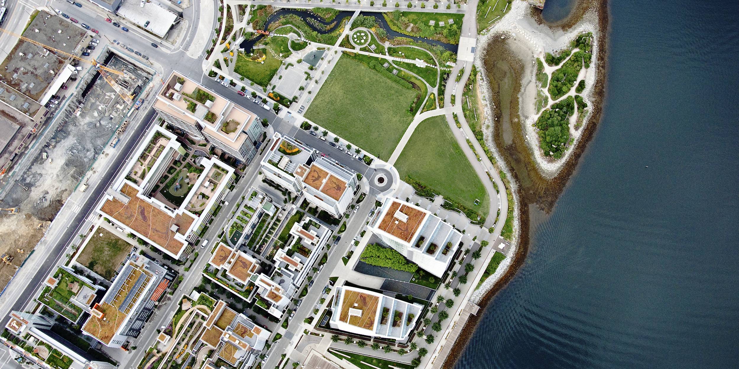 Aerial view of the Southeast False Creek neighbourhood and Hinge Park area. Green roofs are on the high rise buildings in the residential area and Hinge Park contains a wetland and walkways connected to a Habitat island. 
